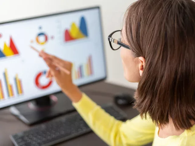 Woman reviewing charts and graphs on a desktop computer.